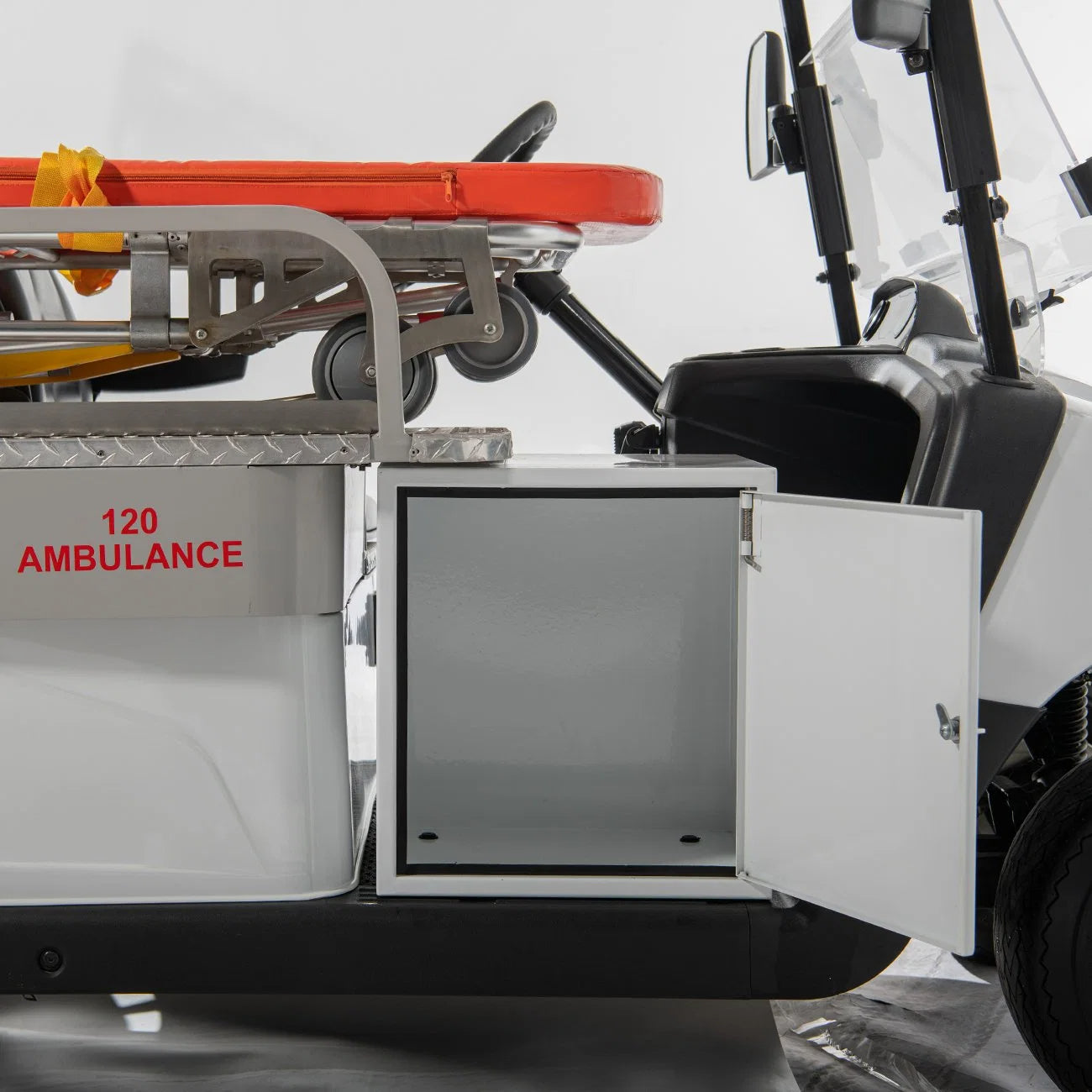UAE golf cartz close-up detail of the storage cabinet on the side of a white ambulance golf cart. The small, white cabinet door is open, revealing the empty interior space for medical supplies. The side panel is labeled "120 AMBULANCE" in red text, with the stretcher visible above, highlighting the specialized medical utility vehicle's practical design for emergency response.