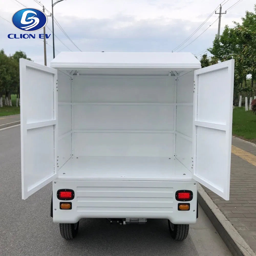 UAE golf cartz rear view of a white enclosed electric delivery vehicle with both back doors wide open, showcasing the empty rear cargo box. This shot highlights the large internal storage capacity and the two fixed interior shelves of the electric utility truck. The last-mile delivery NEV is parked on an asphalt road with a sidewalk and trees in the background.