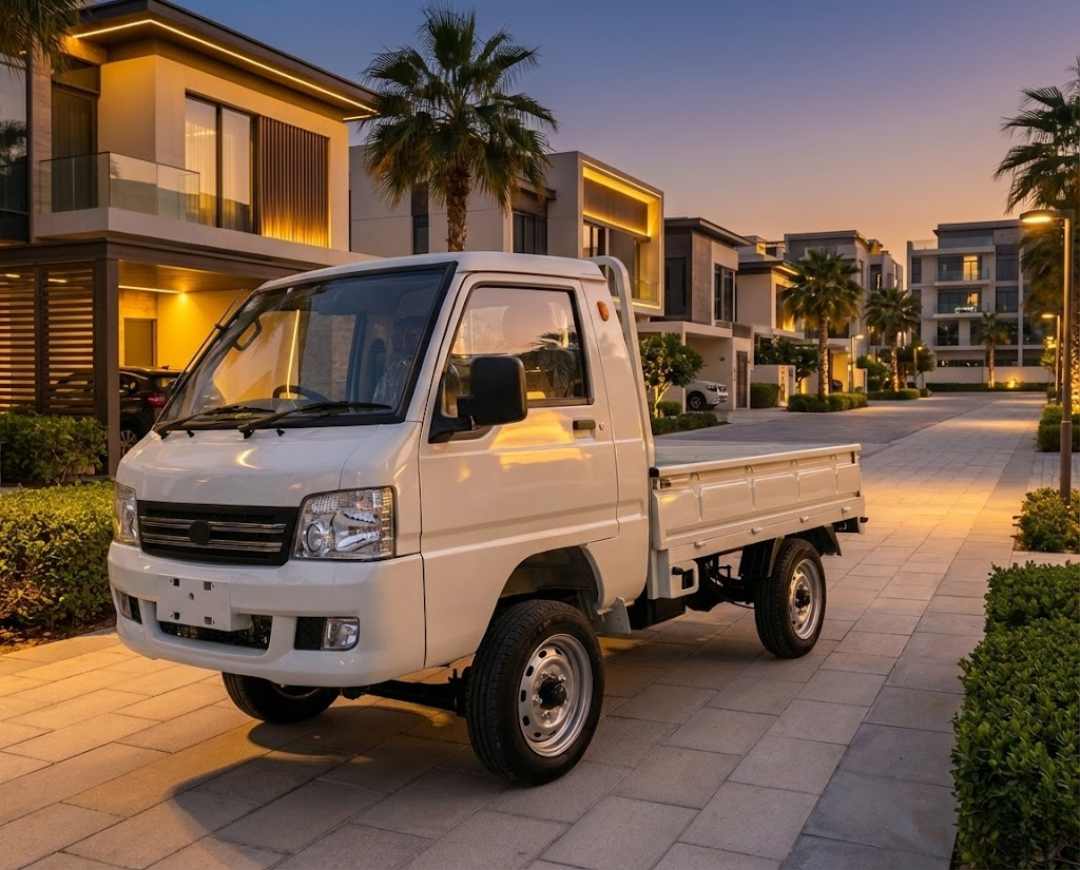 Small white truck parked on a paved area with modern buildings and palm trees in the background.
