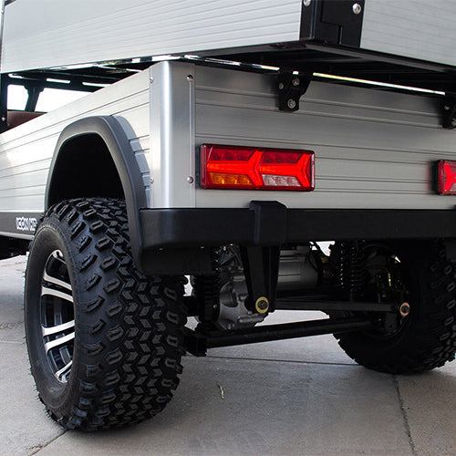 UAE golf cartz close-up rear view of the silver aluminum cargo bed and the off-road tires on a lifted electric utility vehicle. This shot highlights the robust rear suspension, the black and silver custom wheel, and the large, knobby all-terrain tire. The rear panel of the cargo bed features a modern, rectangular LED taillight, emphasizing the heavy-duty and rugged design of the electric work cart.