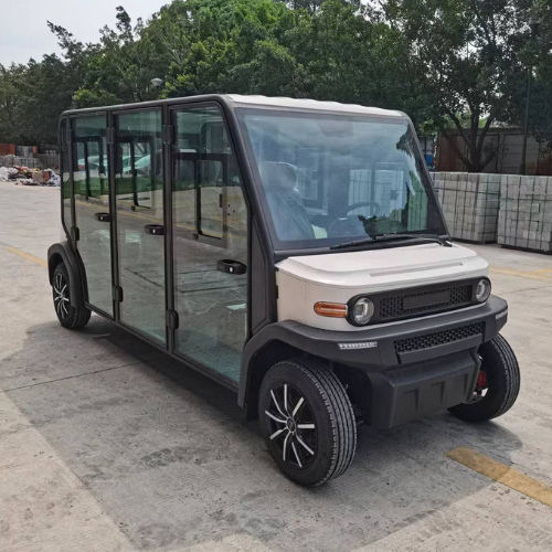 Electric vehicle with glass sides on a paved area with trees in the background