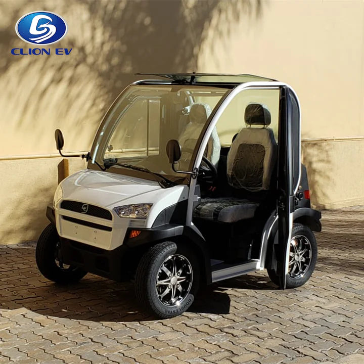 UAE golf cartz three-quarter front view of a white and black two-seater electric vehicle with a fully enclosed cab and a small, tinted roof. This compact NEV or low-speed electric car has a modern front end, black-trimmed doors with clear glass, and black seats. It is equipped with custom black alloy wheels and is parked on a paved stone driveway in a sunny, residential or resort setting.
